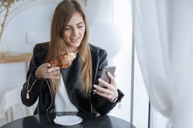 Mujer mirando su móvil mientras se come un croissant