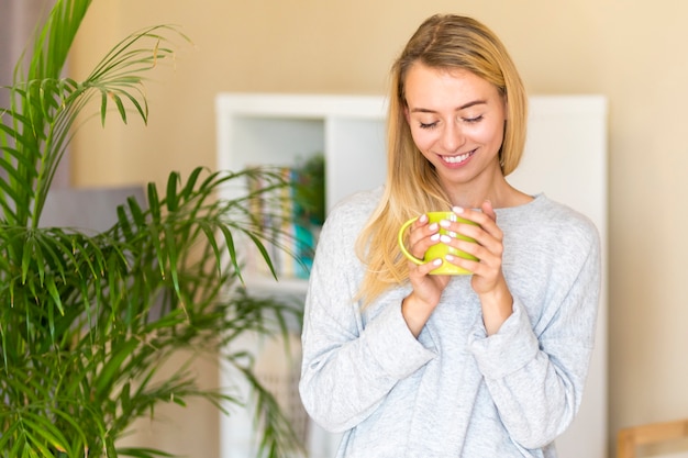 Foto gratuita mujer mirando su taza de café cerca de una planta