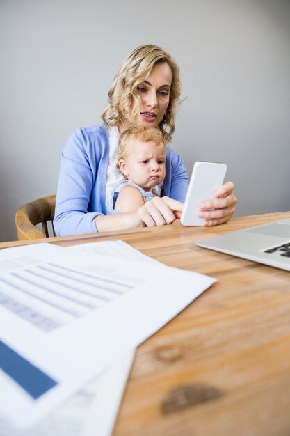 Mujer mirando su teléfono y un bebé con cara de enfado