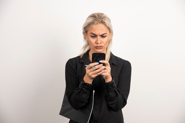 Mujer mirando por teléfono móvil y sosteniendo un portapapeles. Foto de alta calidad