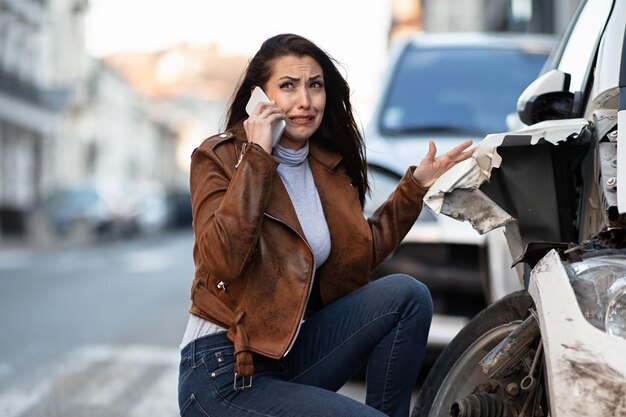 Mujer miserable llorando mientras pide ayuda por teléfono móvil después de un accidente automovilístico