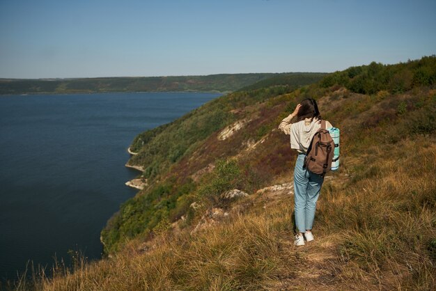 Mujer con mochila caminando por la alta colina verde
