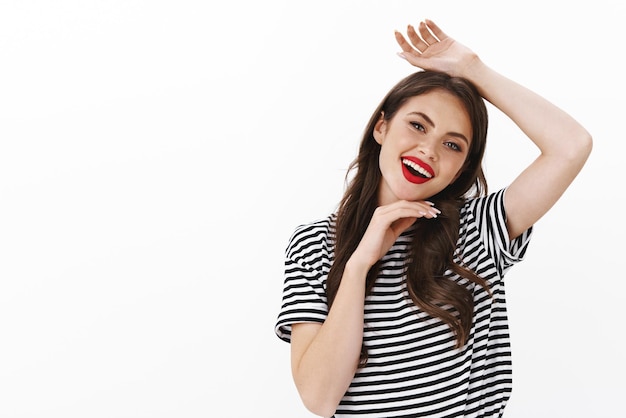 Mujer de moda atractiva y descarada bailando, posando para la cámara, tatuaje, sostén la mano sobre la cabeza, sonrisa coqueta y coqueta