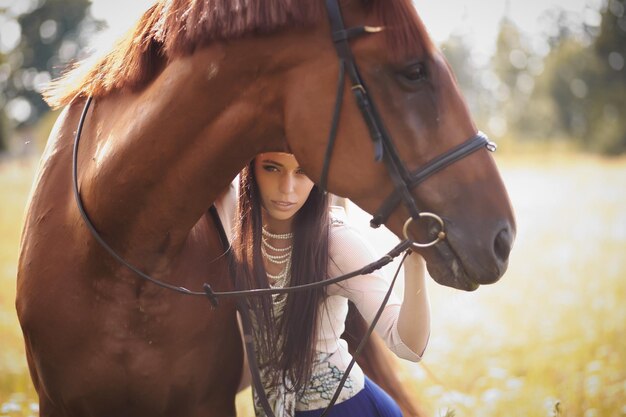 Mujer de moda con cabello castaño largo posando con caballo marrón.