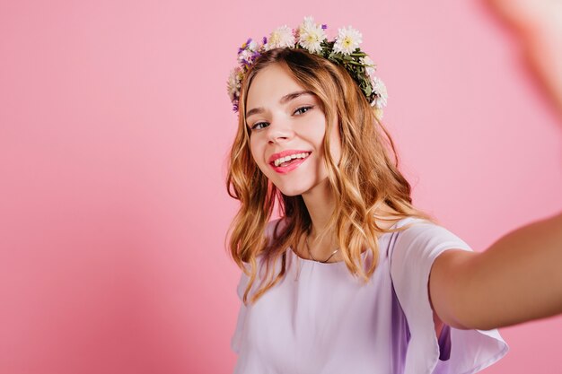 Mujer de moda en corona de flores haciendo selfie con sonrisa suave