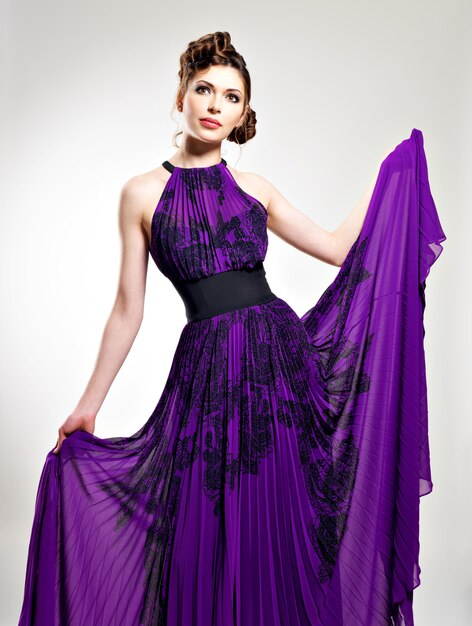 Mujer de moda hermosa en peinado vestido largo púrpura con diseño de coletas, posa en el estudio