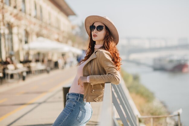 Mujer de moda en jeans casuales disfrutando de la sesión de fotos en la pared del río