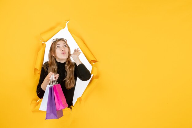 Mujer de moda joven con bolsas de la compra a través del agujero de papel rasgado en la pared