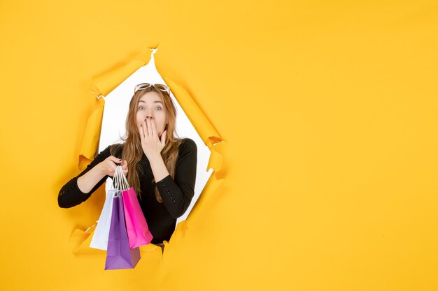 Mujer de moda joven con bolsas de la compra a través del agujero de papel rasgado en la pared