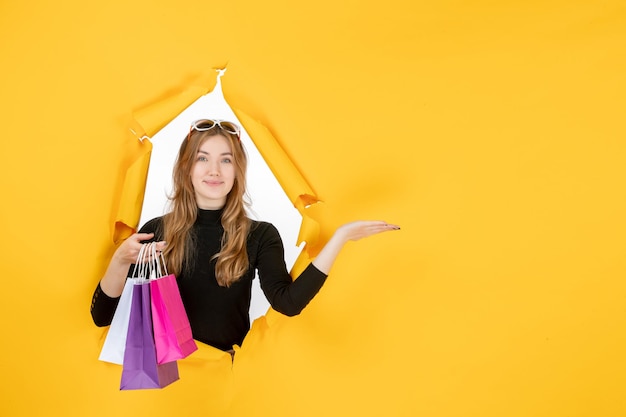 Mujer de moda joven con bolsas de compras a través de un agujero de papel rasgado en la pared