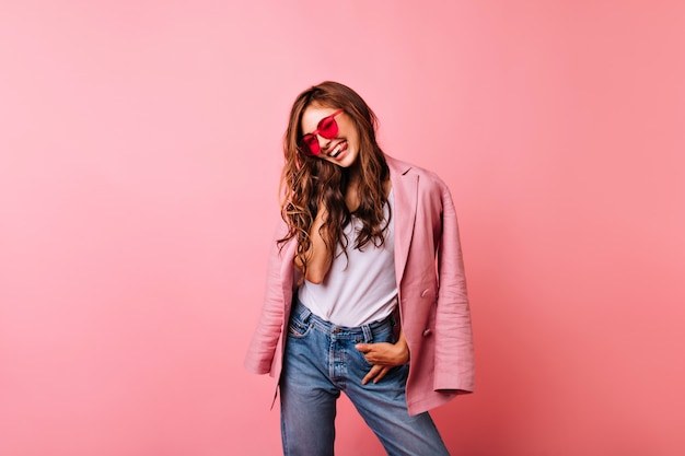 Foto gratuita mujer de moda con pelo largo jengibre feliz riendo. retrato interior de una feliz niña caucásica con gafas de sol de moda y chaqueta rosa.