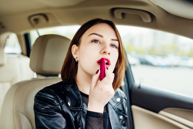 Mujer de moda que compone sus labios con lápiz labial rojo en el coche