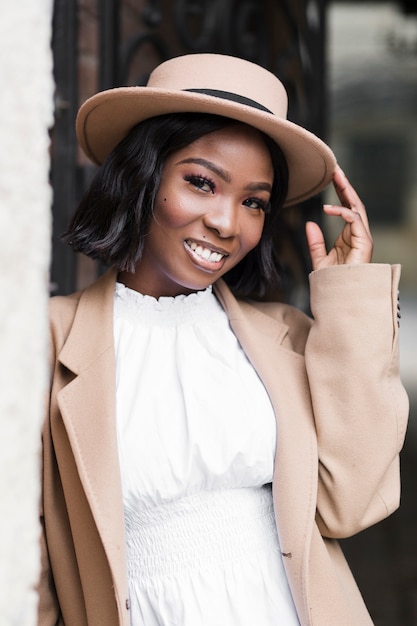 Foto gratuita mujer de moda sonriente posando mientras sostiene su sombrero afuera