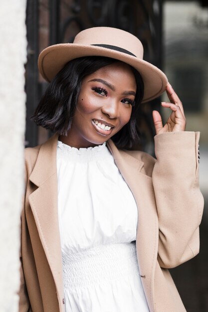 Mujer de moda sonriente posando mientras sostiene su sombrero afuera