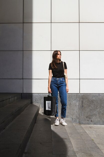 Mujer de la moda de tiro largo posando con una bolsa de compras