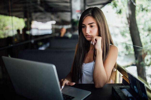 Mujer modelo muy sonriente trabaja en su computadora portátil en la terraza del café daytilme