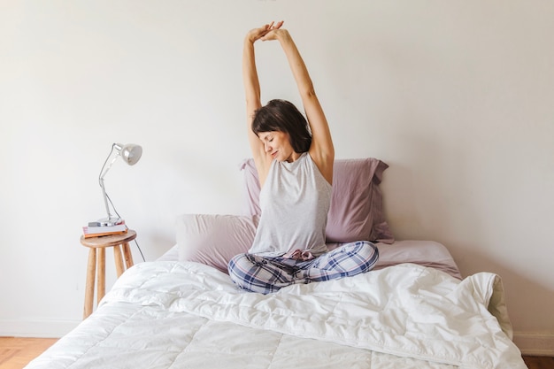 Mujer moderna en cama estirando sus brazos