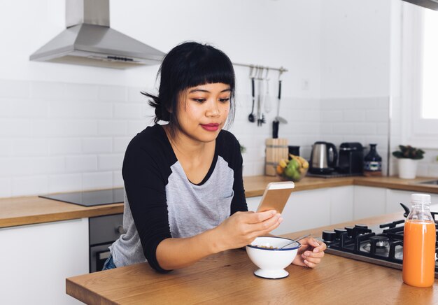 Foto gratuita mujer moderna en la cocina usando el móvil