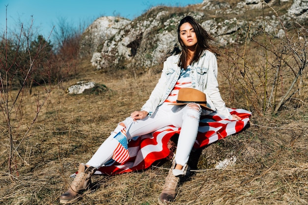 Foto gratuita mujer moderna fresca con bandera estadounidense sentado en la naturaleza