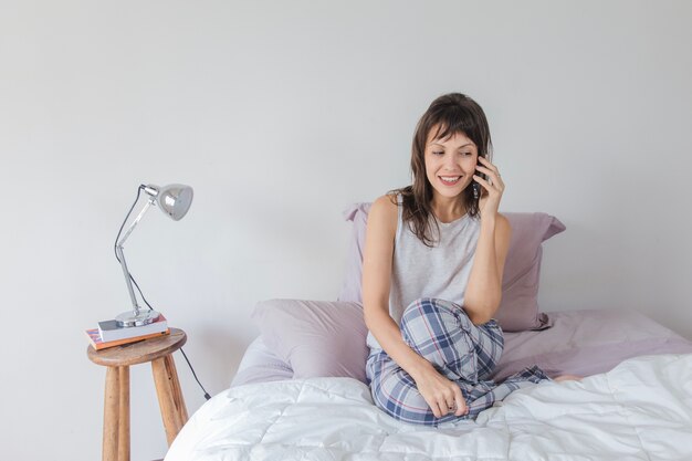 Mujer moderna hablando por smartphone en la cama