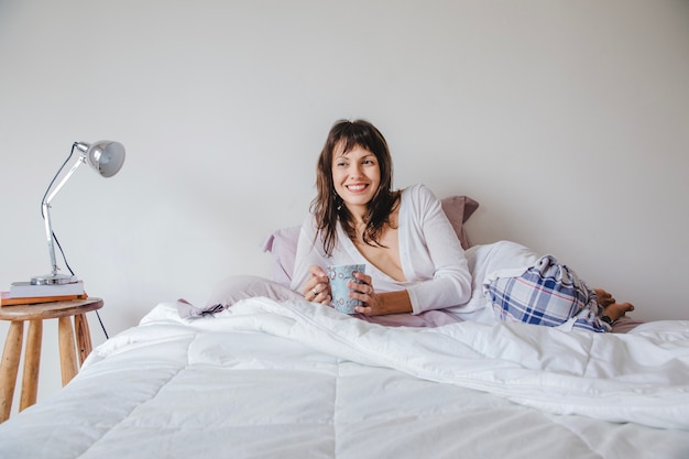Mujer moderna sonriendo con café en la cama