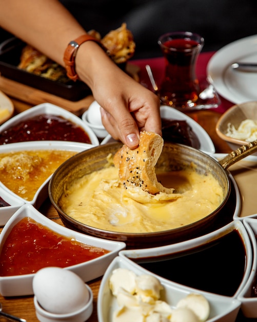 Mujer mojando pan en plato de queso derretido turco servido para el desayuno