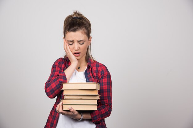 Una mujer molesta mirando una pila de libros en una pared gris.