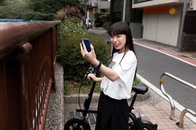 Mujer montando bicicleta en la ciudad y tomando selfie