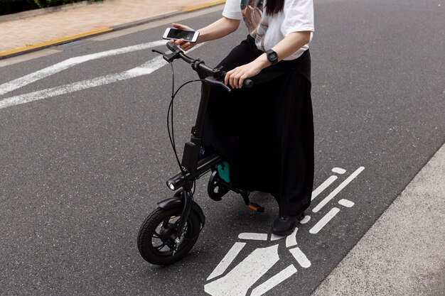 Mujer montando bicicleta eléctrica en la ciudad y sosteniendo smartphone