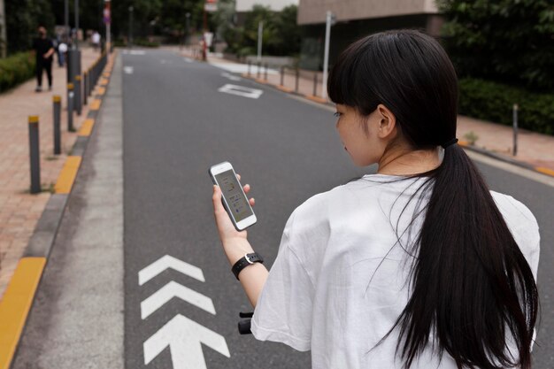 Mujer montando bicicleta eléctrica en la ciudad y sosteniendo smartphone