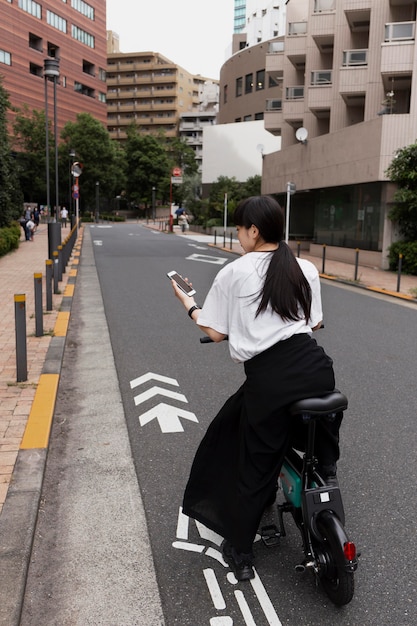 Foto gratuita mujer montando bicicleta eléctrica en la ciudad y sosteniendo smartphone