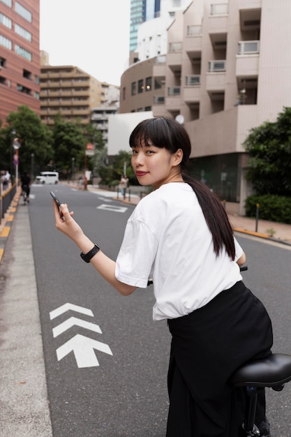 Foto gratuita mujer montando bicicleta eléctrica en la ciudad y sosteniendo smartphone