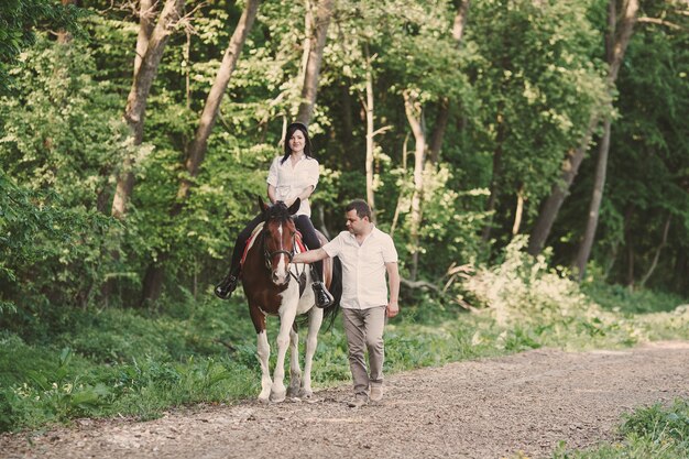 Mujer montando a caballo y su marido a pie