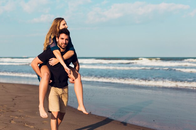 Mujer montando en la parte posterior del hombre en la playa