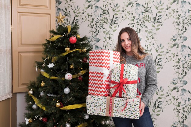 Mujer, con, montón, de, regalos, cerca, árbol de navidad