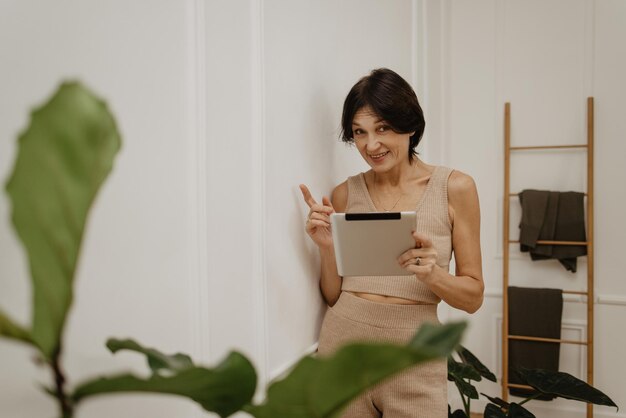 Mujer morena adulta caucásica trabajando en proyecto en tableta en habitación con plantas Concepto remoto