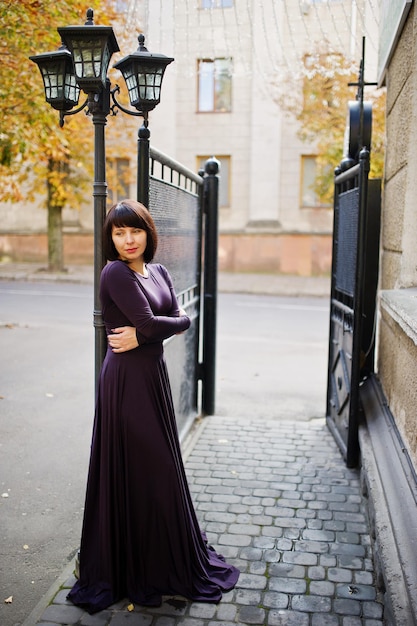 Mujer morena adulta en puertas de hierro negro de fondo vestido violeta