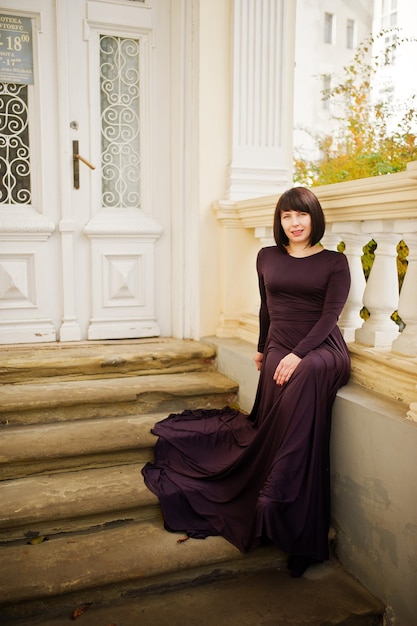 Mujer morena adulta en el vestido violeta fondo antigua casa vintage con escaleras