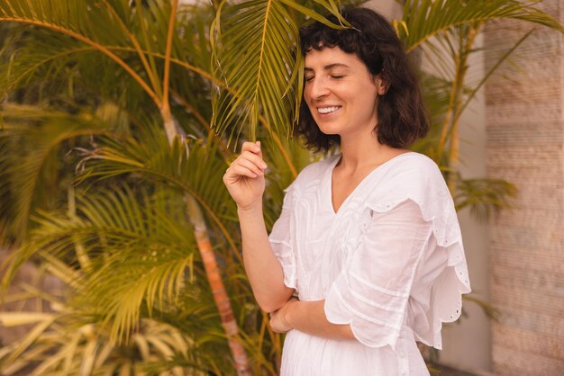 Mujer morena caucásica bastante joven en vestido blanco cerrando los ojos disfruta del clima de verano al aire libre