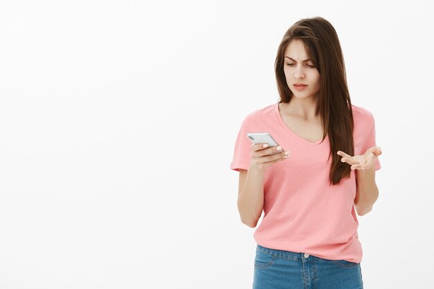 Mujer morena confundida posando en el estudio con su teléfono