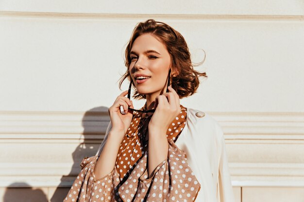 Mujer morena curiosa con sonrisa suave. Tiro al aire libre de la muchacha bastante caucásica con gafas de sol.