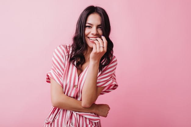 Mujer morena emocionada lleva anillo sonriendo. Foto interior de una hermosa chica de pelo oscuro con un elegante vestido a rayas.