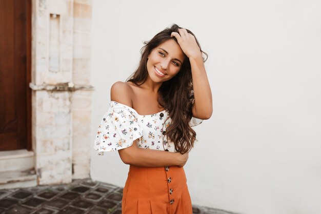 Mujer morena está sonriendo dulcemente contra el edificio antiguo