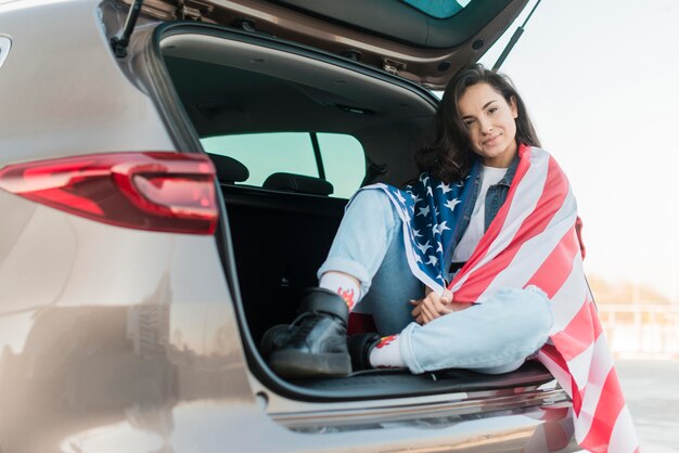 Mujer morena con gran bandera de Estados Unidos en el baúl del auto