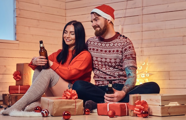 Mujer morena y hombre hipster barbudo beben cerveza y celebran la Navidad en casa.