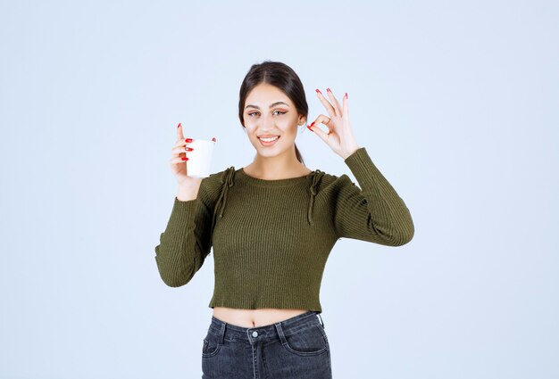 Mujer morena joven que da la muestra aceptable para el té en el fondo blanco.