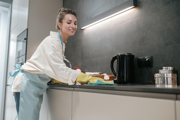 Mujer morena joven que limpia las superficies en la cocina