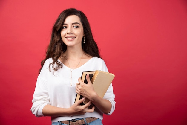 Mujer morena con libros sobre fondo rojo. Foto de alta calidad