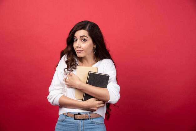 Mujer morena con libros sobre fondo rojo. Foto de alta calidad