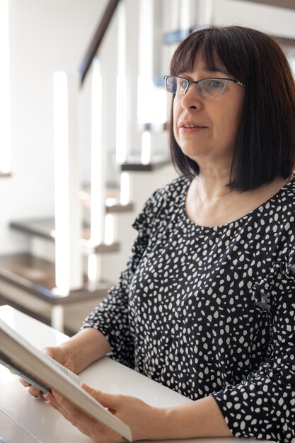 Una mujer morena de mediana edad con gafas y un corte de pelo bob está leyendo un libro